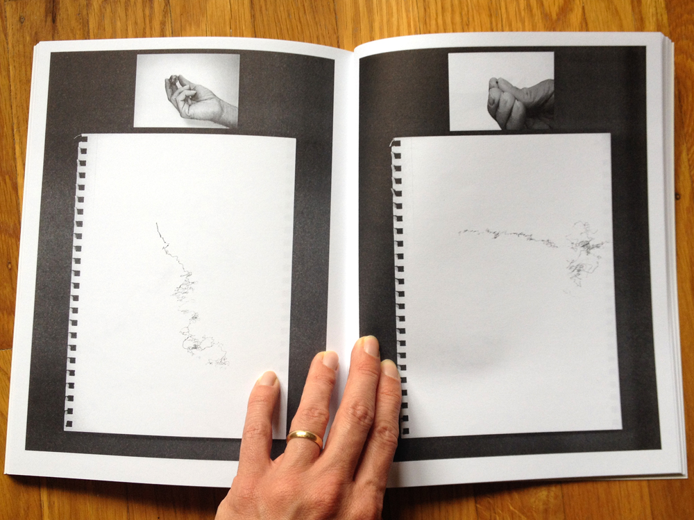 A book held open, images on each page showing a hand holding a stone (left) and a moonrock (right) with corresponding gestural drawing