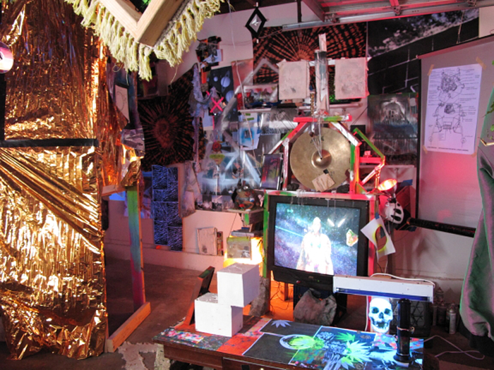 A cacophonous visual scene inside the garage with a television, many posters, amd a gold-foil wrapped room