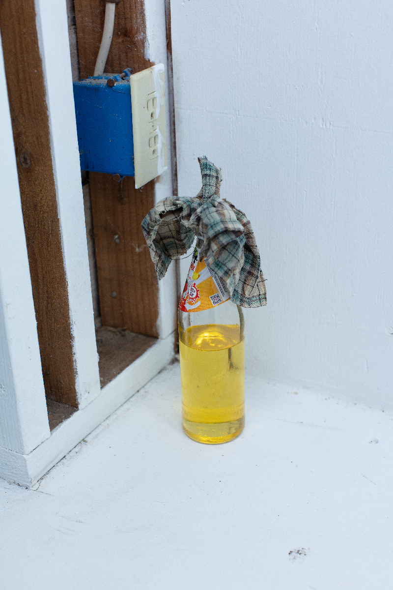A glass bottle partially filled with yellow liquid, a plaid rag stuffed in its neck.