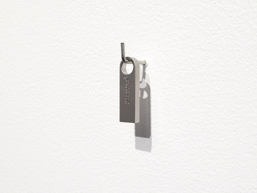 a small metal flash drive hanging on a metal hook attached ot a wall